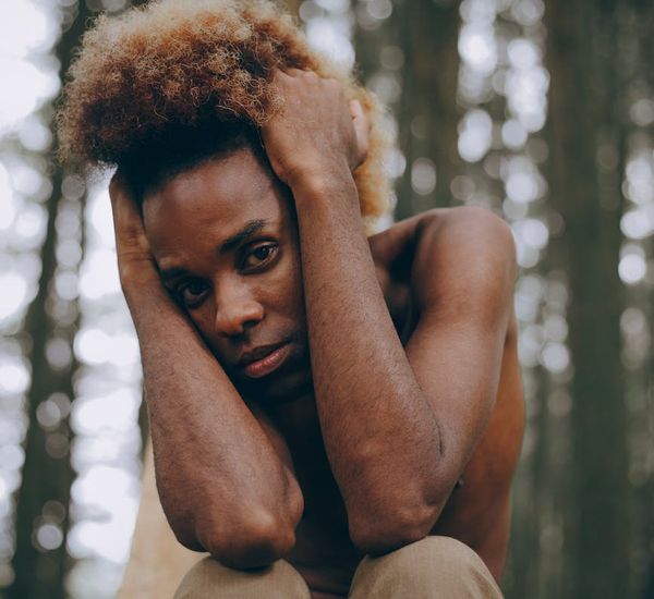 A person sitting in a meditative pose with a calm expression, outdoors in nature.